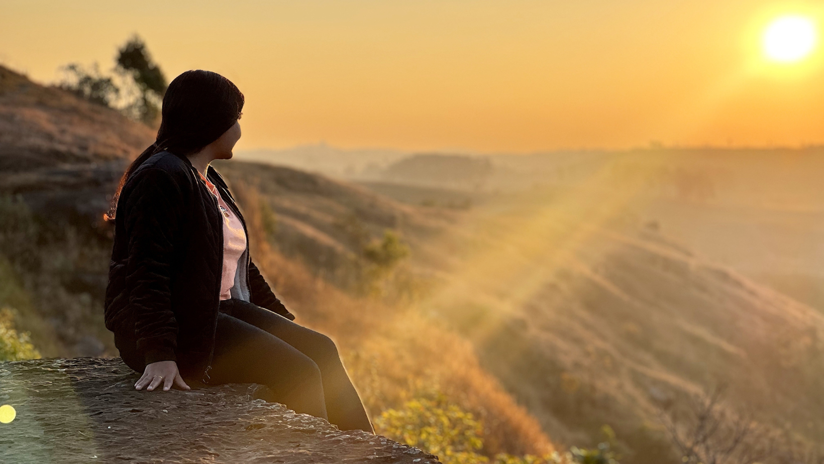 Person sitting outdoors at sunset and looking across the landscape